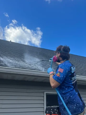 A professional pressure washer soft washing a roof with an algaecide solution in Peoria, IL.
